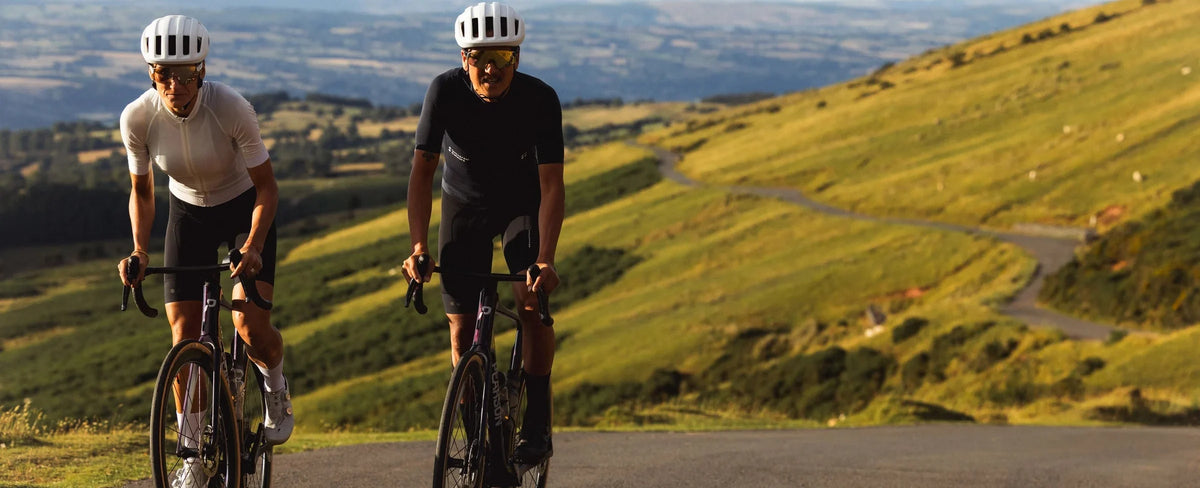 Two riders on Pearson Forge bikes climbing a road above a green valley